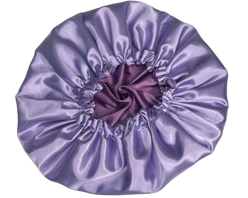 Op de afbeelding: Een lavendel satijnen muts met een paarse satijnen voering. De muts is bovenaan gerimpeld en heeft een gladde, zijdeachtige textuur.