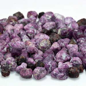以下が含まれることがあります： 紫と濃い赤色の小さなざらざらした宝石の山。宝石は不規則な形をしていて、自然な研磨されていない外観をしています。