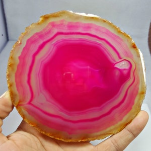 May include: A pink agate slice with white and yellow banding. The agate is polished and has a smooth surface.