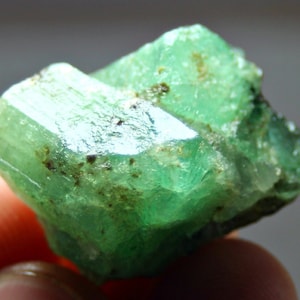 May include: A vibrant green emerald crystal with a rough, natural texture. The crystal has a deep, rich green color and is translucent. It is a beautiful example of a natural emerald.