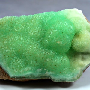 May include: A green and white mineral specimen with a rough, textured surface. The mineral has a crystalline structure and appears to be a type of calcite.