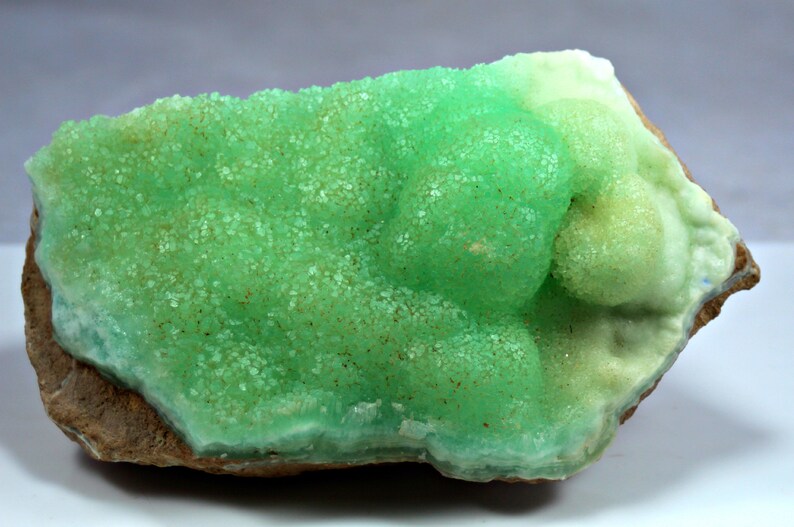 May include: A green and white mineral specimen with a rough, textured surface. The mineral has a crystalline structure and appears to be a type of calcite.