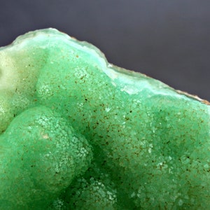 May include: A close-up of a green and white mineral specimen with a rough, textured surface. The mineral has a bubbly, rounded shape and appears to be a geode.
