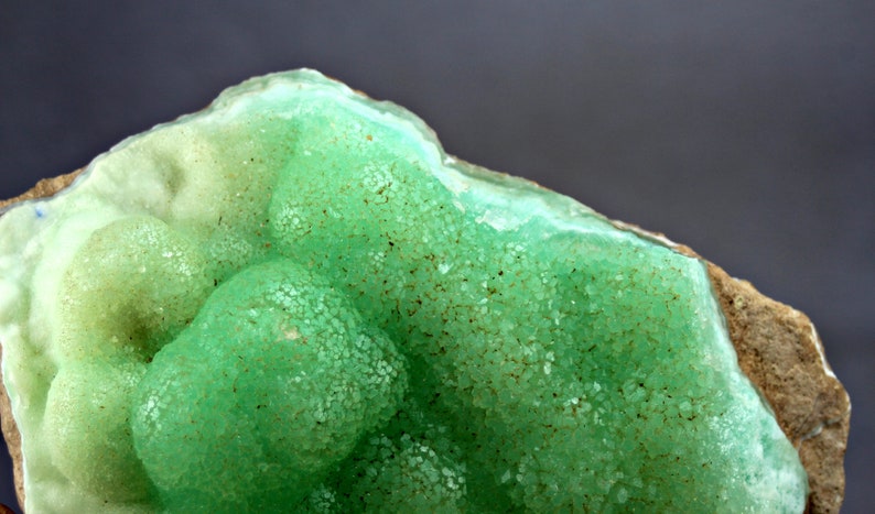 May include: A close-up of a green and white mineral specimen with a rough, textured surface. The mineral has a bubbly, rounded shape and appears to be a geode.