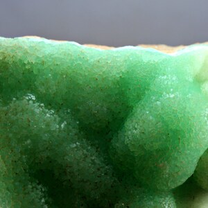 May include: A green and white mineral specimen with a rough, textured surface. The mineral is a geode, which is a hollow rock lined with crystals.