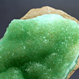 May include: A close-up of a green mineral specimen with a rough, textured surface. The mineral is a cluster of small, green crystals.