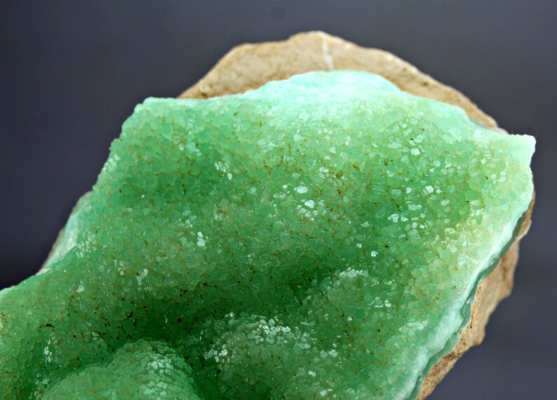 May include: A close-up of a green mineral specimen with a rough, textured surface. The mineral is a cluster of small, green crystals.