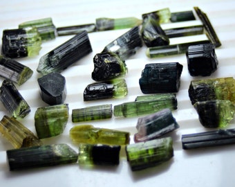 May include: A collection of green, black, and brown tourmaline crystals. The crystals are raw and have a variety of shapes and sizes.
