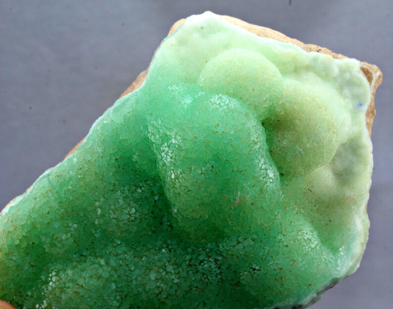 May include: A green and white mineral specimen with a rough, textured surface. The mineral has a bubbly, rounded shape and is a natural formation.