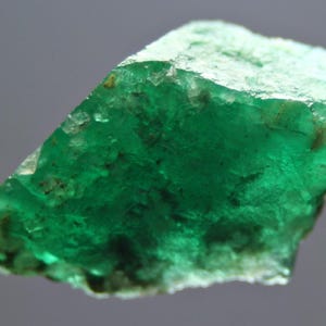 May include: A large, rough, green emerald gemstone with a natural, irregular shape.