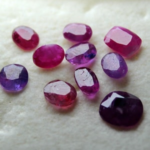 May include: Assortment of pink and purple gemstones, some oval shaped, some round, some with a faceted finish.