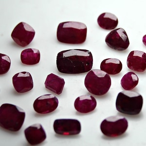 Könnte beinhalten: Eine Sammlung von 20 losen, facettierten, roten Edelsteinen. Die Edelsteine sind in verschiedenen Formen und Größen und sind in einem Kreis auf einer weißen Oberfläche angeordnet.