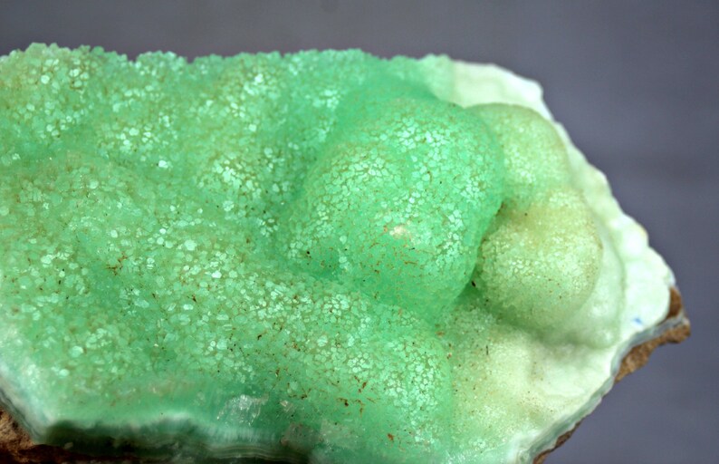 May include: A green and white mineral specimen with a rough, textured surface. The mineral has a botryoidal shape, with rounded, bulbous formations.