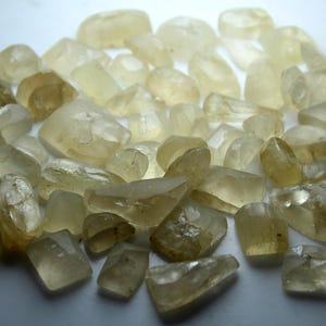 May include: A collection of translucent, pale yellow, faceted gemstones. The stones are of various sizes and shapes, with some having a more rounded shape and others being more angular.