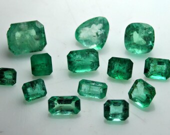 May include: A collection of emerald gemstones in various shapes, including rectangular, square, and oval cuts. The gemstones are a vibrant green color and are displayed on a white surface.