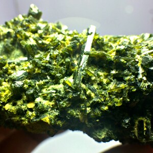 May include: A cluster of green and yellow crystals, with a rough, textured surface. The crystals are arranged in a dense, compact formation.