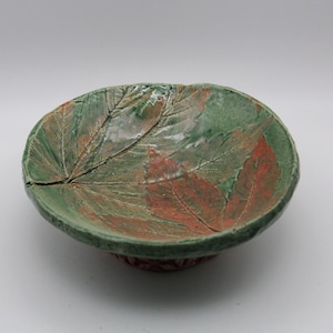 May include: A small ceramic bowl with a green glaze and a design of leaves in shades of green and orange.