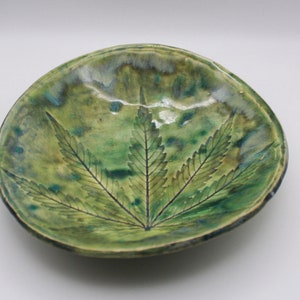 May include: A green ceramic dish with a raised leaf design. The dish has a mottled green glaze with hints of blue and brown.