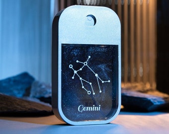 May include: A silver and black Gemini zodiac sign keychain with a clear background and a silver ring. The keychain features a constellation of stars and the word "Gemini" printed in white.