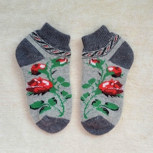 May include: A pair of grey ankle socks with a floral pattern. The socks feature red roses with green leaves and stems. The top and heel are a darker grey with a decorative pattern.