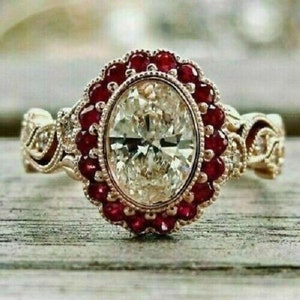 May include: An ornate gold ring featuring an oval-cut, clear gemstone surrounded by small, round, red gemstones. The ring has a detailed, filigree design on the band and around the central stone, showcasing a vintage or antique style.