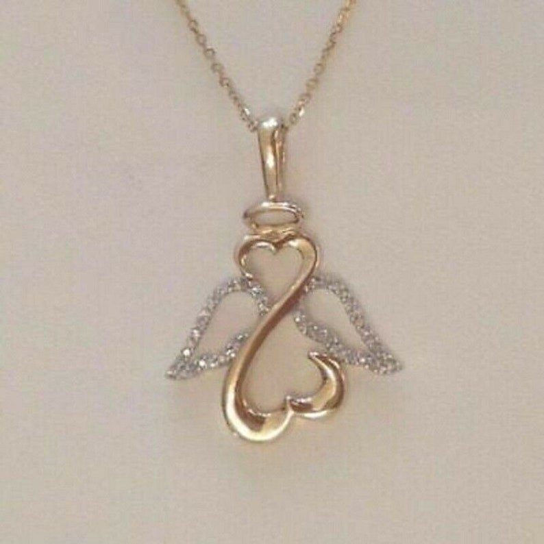 May include: A gold pendant necklace with a heart-shaped design and angel wings. The wings are adorned with small, clear stones.