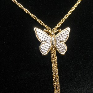 May include: A gold-coloured butterfly pendant necklace. The butterfly has a silver-coloured dotted pattern on its wings and a gold-coloured body. The necklace chain is also gold-coloured, with two dangling chains below the butterfly.