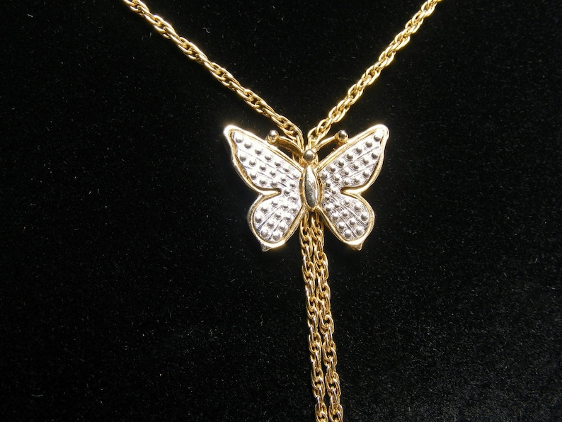 May include: A gold-coloured butterfly pendant necklace. The butterfly has a silver-coloured dotted pattern on its wings and a gold-coloured body. The necklace chain is also gold-coloured, with two dangling chains below the butterfly.