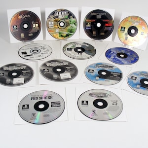 May include: A collection of PlayStation 1 video game discs, each in a white paper sleeve. The discs feature various game titles, including "Hexen," "Army Men," and "Tony Hawk's Pro Skater." The discs are silver with black text and graphics.