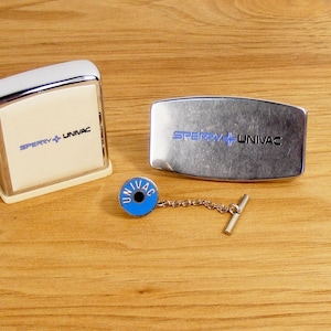May include: Two silver metal boxes with the text "Sperry + Univac" on them. A silver tie tack with a blue circle and the text "Univac" on it.