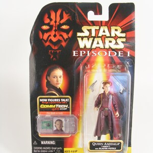 May include: A Star Wars Episode I action figure of Queen Amidala in a burgundy robe with blaster pistols. The figure is packaged in a plastic blister pack with a red and black background featuring Darth Maul's face. The packaging also includes a small clear plastic card with a picture of Queen Amidala and the text "NOW FIGURES TALK! Through a special reader with a COMMTECH CHIP".