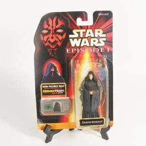 May include: A Star Wars Episode I action figure of Darth Sidious in a black robe with a red lightsaber. The figure is packaged in a cardboard box with a red and black background. The box also features a picture of Darth Maul.