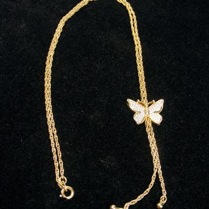 May include: A gold necklace featuring a butterfly pendant. The butterfly is adorned with small, sparkling stones. The necklace has a delicate chain and a clasp. The butterfly pendant is approximately 2 cm wide.
