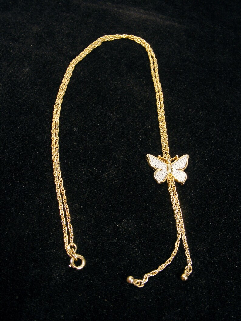 May include: A gold necklace featuring a butterfly pendant. The butterfly is adorned with small, sparkling stones. The necklace has a delicate chain and a clasp. The butterfly pendant is approximately 2 cm wide.