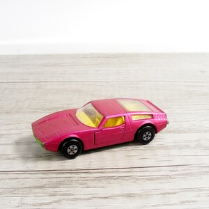 May include: A vintage toy car in a vibrant pink hue, featuring a sleek design with a yellow interior and transparent roof panels. The car has black wheels and green accents, evoking a sense of classic toy car nostalgia.