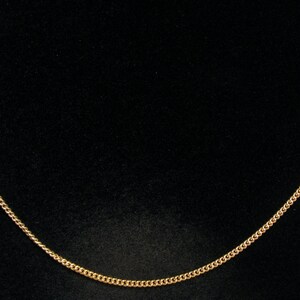 May include: A delicate gold necklace with a curb chain and small, round beads. The necklace is displayed against a black background, highlighting its simple elegance. The chain is approximately 45 cm long.