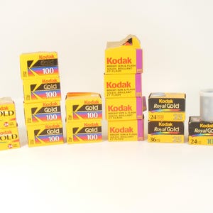 May include: A collection of Kodak film boxes including Gold 100, Bright Sun & Flash 200, and Royal Gold 25 and 1000 varieties. The yellow and black cardboard boxes feature colorful graphic accents and text indicating film speed and exposure counts.