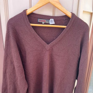 May include: A brown v-neck sweater with long sleeves. The sweater has a label that reads "LAND made".