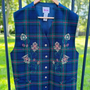 May include: A blue, green, and red plaid vest with embroidered floral designs in gold and green. The vest has a  "Tan Jay" label on the inside.