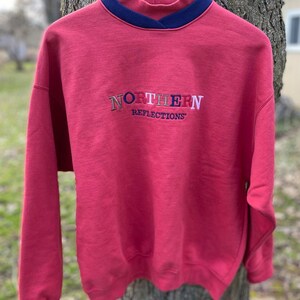 May include: Red sweatshirt with a mock neck and a multi-colored embroidered logo that says "NORTHERN REFLECTIONS"