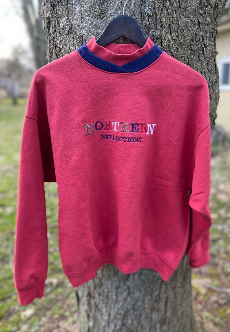 May include: Red sweatshirt with a mock neck and a multi-colored embroidered logo that says "NORTHERN REFLECTIONS"