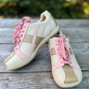 K&ouml;nnte beinhalten: Ein Paar Canvas-Sneaker mit rosa und braunen Akzenten. Die Schn&uuml;rsenkel sind rosa und die Schuhe haben eine wei&szlig;e Sohle.