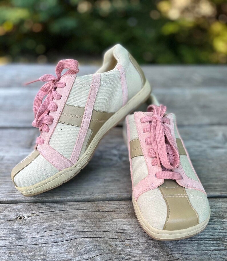 K&ouml;nnte beinhalten: Ein Paar Canvas-Sneaker mit rosa und braunen Akzenten. Die Schn&uuml;rsenkel sind rosa und die Schuhe haben eine wei&szlig;e Sohle.
