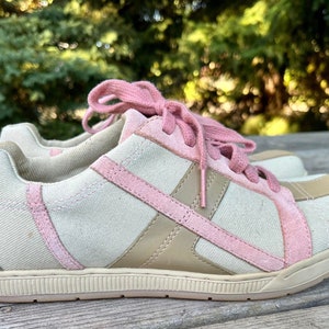 K&ouml;nnte beinhalten: Ein Paar niedrige Sneakers mit beigefarbenem Canvas-Obermaterial und rosa Wildlederakzenten. Die Schn&uuml;rsenkel sind rosa und die Sohle ist wei&szlig;.