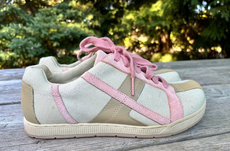 K&ouml;nnte beinhalten: Ein Paar niedrige Sneakers mit beigefarbenem Canvas-Obermaterial und rosa Wildlederakzenten. Die Schn&uuml;rsenkel sind rosa und die Sohle ist wei&szlig;.