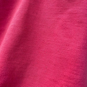 May include: Close-up of a smooth, pink fabric with a slight sheen. The fabric has a subtle texture and a uniform color.