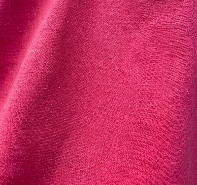 May include: Close-up of a smooth, pink fabric with a slight sheen. The fabric has a subtle texture and a uniform color.