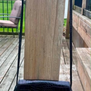 May include: Black crossbody bag with a textured, crocodile-like pattern. The bag features a silver heart-shaped clasp and a black rope strap with silver accents. The bag is hanging on a wooden post.
