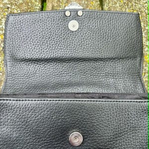May include: Black leather handbag with a textured surface. The bag features a silver-colored clasp and a magnetic snap closure. The interior is lined with black fabric.