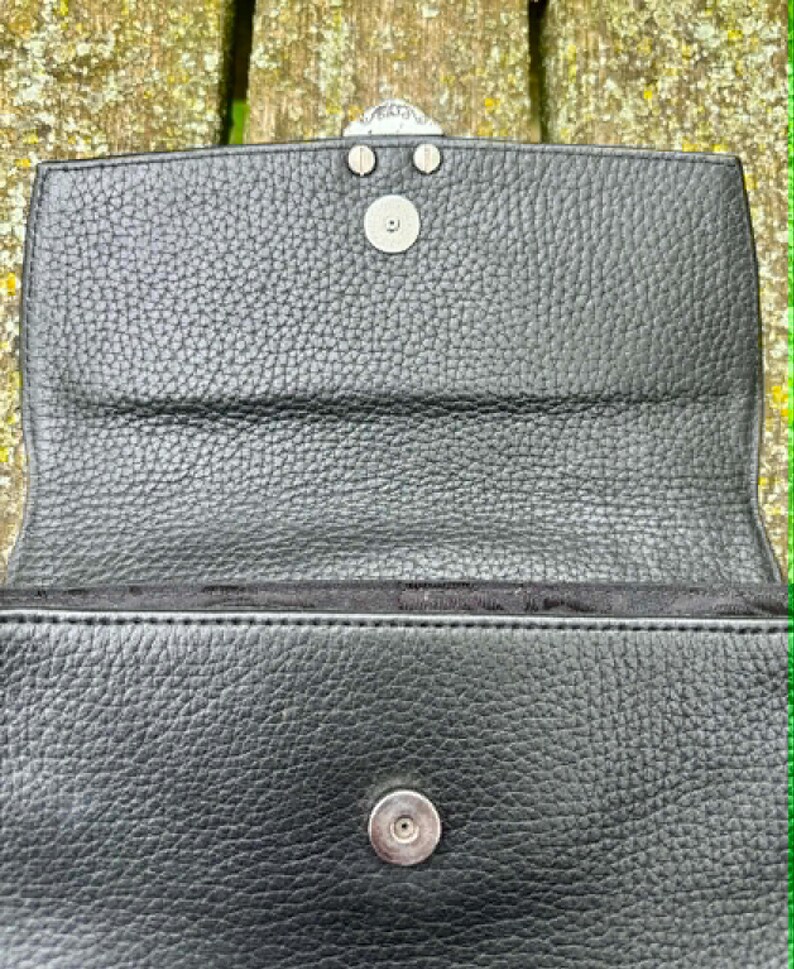 May include: Black leather handbag with a textured surface. The bag features a silver-colored clasp and a magnetic snap closure. The interior is lined with black fabric.